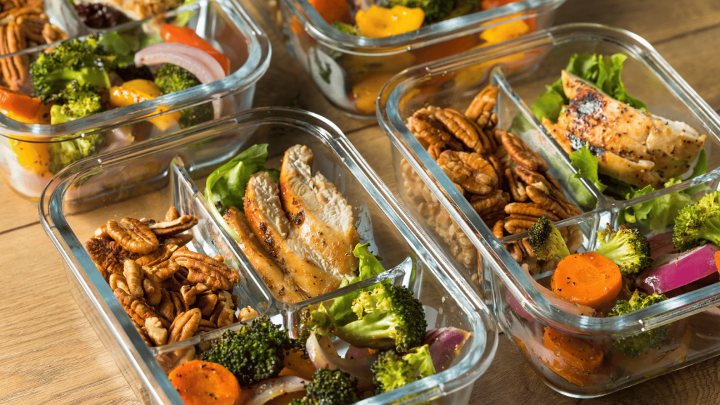 This image displays a variety of nutritious meals from a prepared meal delivery service, neatly packed in clear glass containers. Each container holds a balanced meal, featuring a combination of grilled chicken breast on a bed of lettuce, a mix of roasted vegetables like broccoli and carrots, and a portion of pecans for added crunch and nutrition. The meals are well-portioned, highlighting the convenience and balanced nutrition provided by prepared meal delivery services
