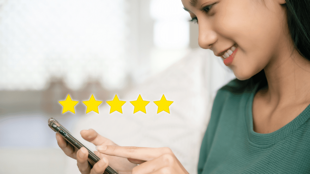 This image shows a smiling woman looking at her smartphone with a row of five bright yellow stars displayed on the screen above her. The stars suggest she is reviewing a service, symbolizing a positive customer experience. This visual is ideal for the customer reviews section of a website highlighting the best prepared meal delivery service, reflecting high customer satisfaction and excellent ratings.