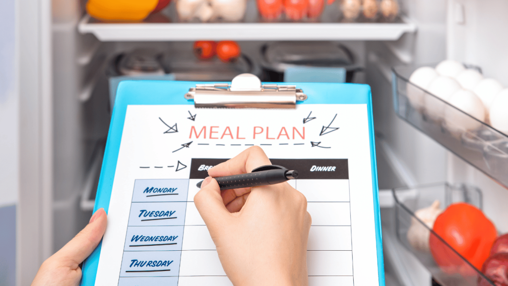 The image displays a close-up of a person's hand holding a pen, poised to write on a meal plan clipboard. The clipboard contains a chart labeled "Meal Plan" with sections for breakfast, lunch, and dinner from Monday to Thursday, some of which are already checked off, indicating completed planning. The background subtly reveals an open refrigerator stocked with fresh produce like eggs and vegetables, highlighting the importance of meal planning. This image encapsulates the concept of meal planning as a strategic tool for saving money on groceries and maximizing a budget, and can be effectively used in the section "The Power of Meal Planning" for the article "Supermarket Shopping Strategies: How to Save Money on Groceries and Maximize Your Budget".